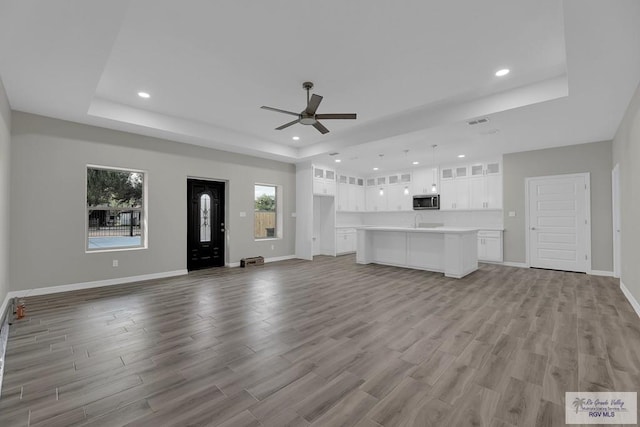 unfurnished living room featuring a raised ceiling, ceiling fan, and light hardwood / wood-style floors