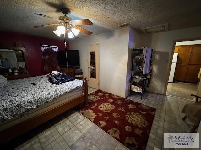 bedroom featuring ceiling fan, refrigerator, and a textured ceiling