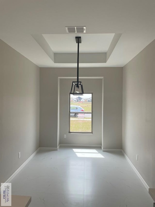 empty room with a tray ceiling, visible vents, and baseboards