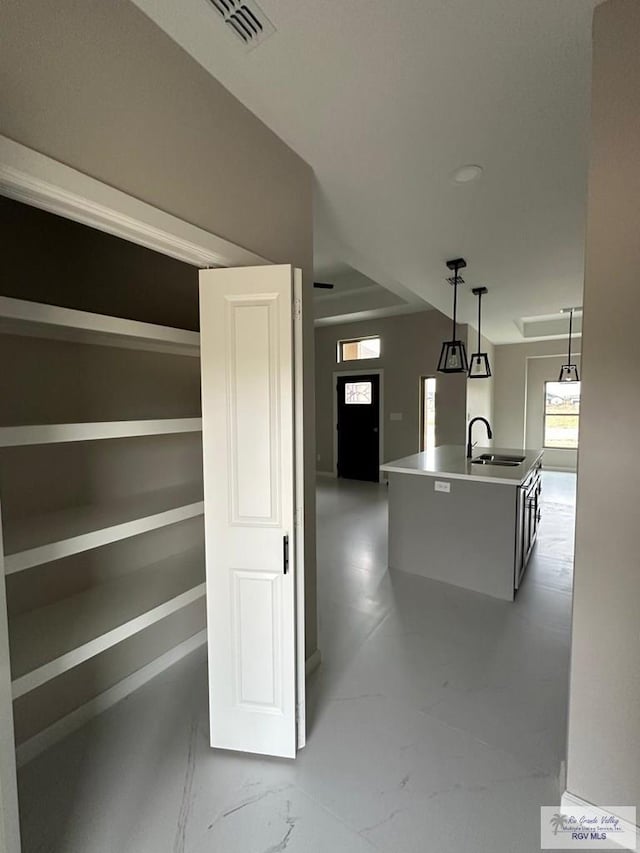 kitchen featuring a kitchen island with sink, a sink, visible vents, marble finish floor, and decorative light fixtures