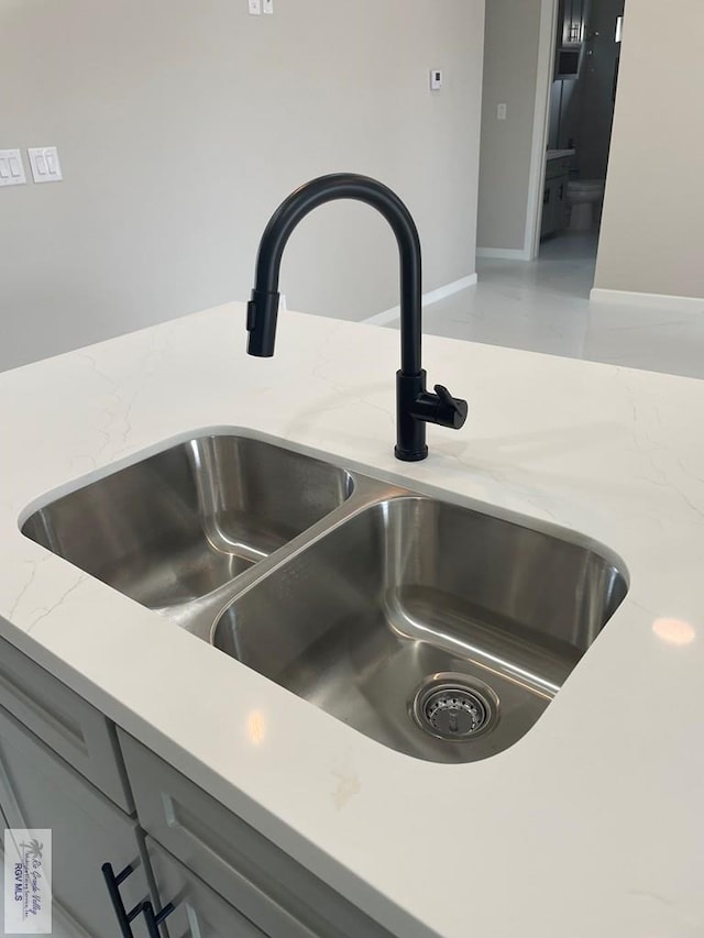 room details featuring baseboards, a sink, light stone countertops, and gray cabinetry