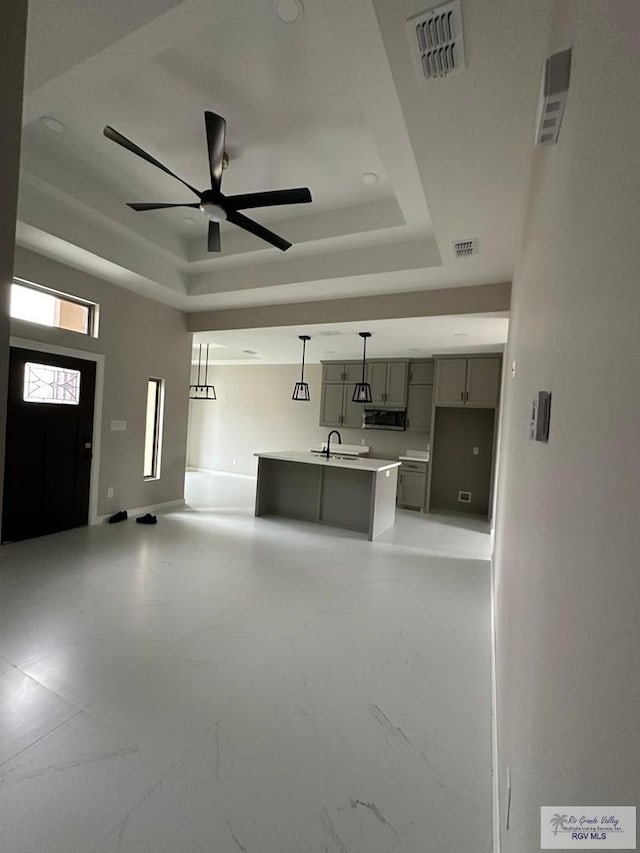 unfurnished living room with a raised ceiling, visible vents, ceiling fan, and a sink