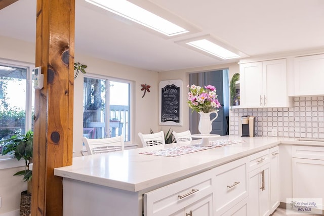 kitchen featuring kitchen peninsula, decorative backsplash, and white cabinetry