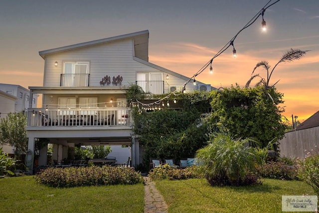 back house at dusk featuring a yard and a balcony