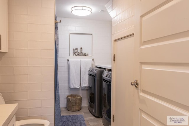 bathroom with walk in shower, vanity, washer and dryer, tile walls, and toilet