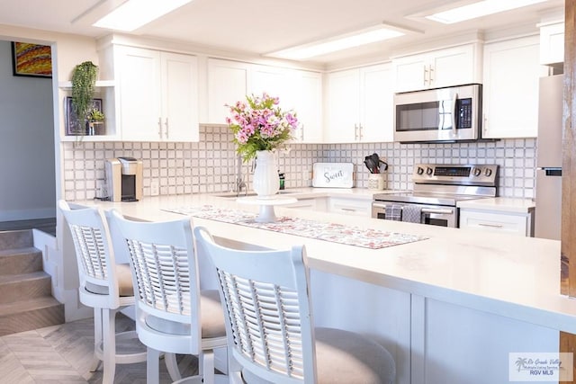 kitchen with white cabinets, appliances with stainless steel finishes, a breakfast bar, and tasteful backsplash