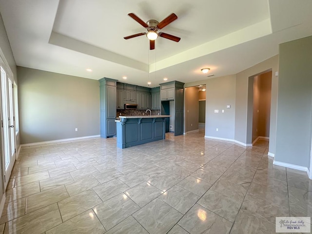 kitchen featuring a kitchen bar, a tray ceiling, a kitchen island, ceiling fan, and decorative backsplash