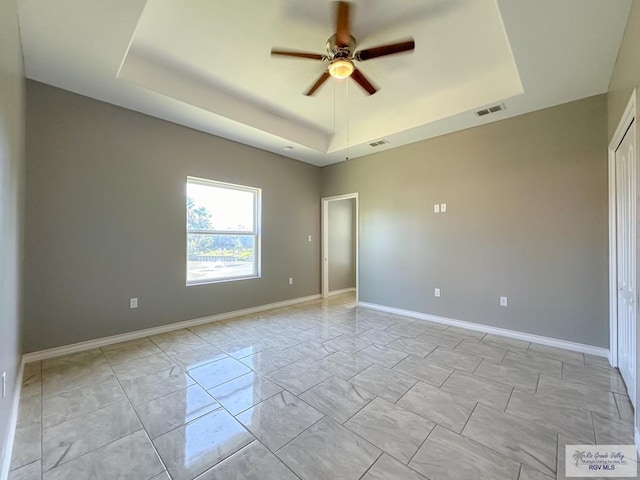 empty room with ceiling fan and a raised ceiling