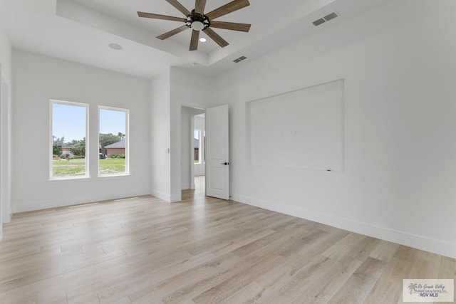 unfurnished room featuring ceiling fan, light wood finished floors, baseboards, visible vents, and a raised ceiling