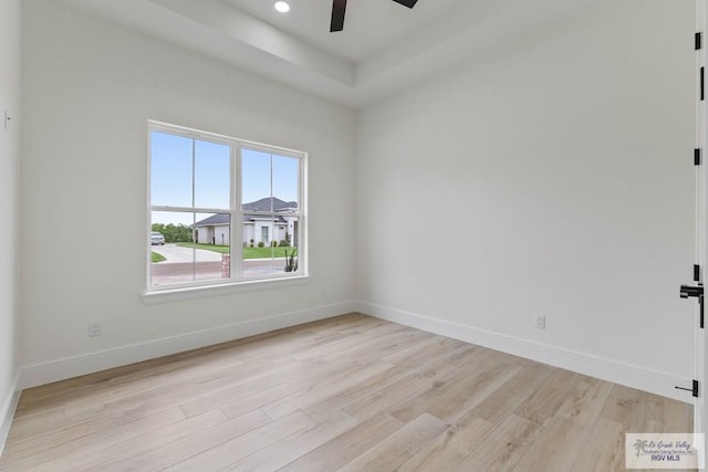 empty room with ceiling fan, baseboards, a raised ceiling, and light wood-type flooring