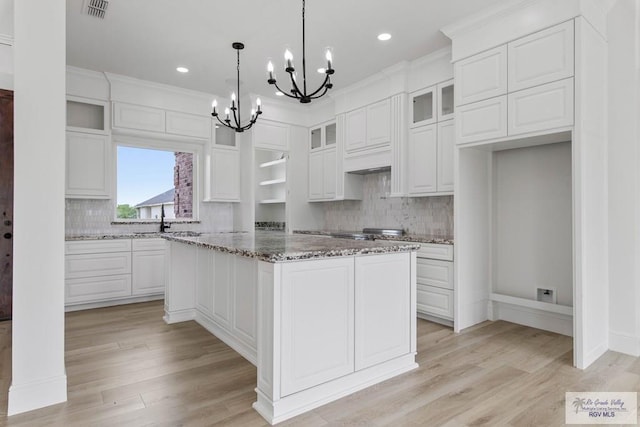 kitchen featuring decorative backsplash, white cabinets, glass insert cabinets, visible vents, and an inviting chandelier