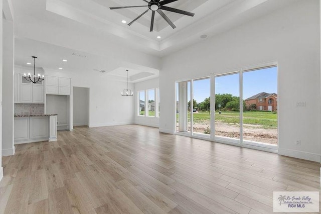 unfurnished living room with recessed lighting, light wood-style floors, a raised ceiling, baseboards, and ceiling fan with notable chandelier
