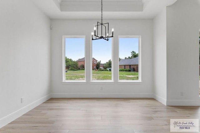 unfurnished dining area with plenty of natural light, an inviting chandelier, light wood-style floors, and a tray ceiling