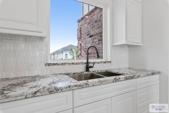 kitchen featuring white cabinets, backsplash, light stone countertops, and a sink