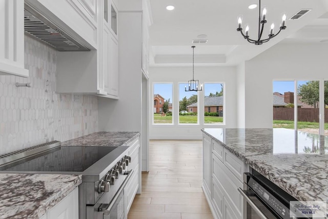 kitchen featuring wall chimney range hood, visible vents, stainless steel appliances, plenty of natural light, and an inviting chandelier