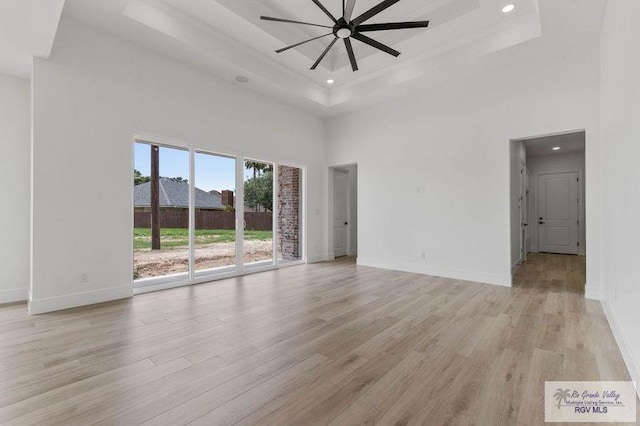 unfurnished living room featuring light wood-style flooring, a raised ceiling, baseboards, recessed lighting, and a high ceiling