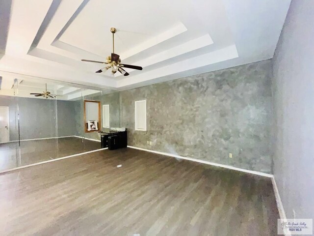 empty room with wood-type flooring, a tray ceiling, and ceiling fan