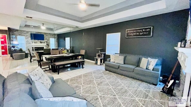 tiled living room with ceiling fan and a raised ceiling