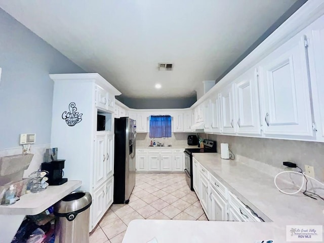 kitchen featuring stainless steel refrigerator with ice dispenser, black electric range oven, sink, light tile patterned floors, and white cabinetry