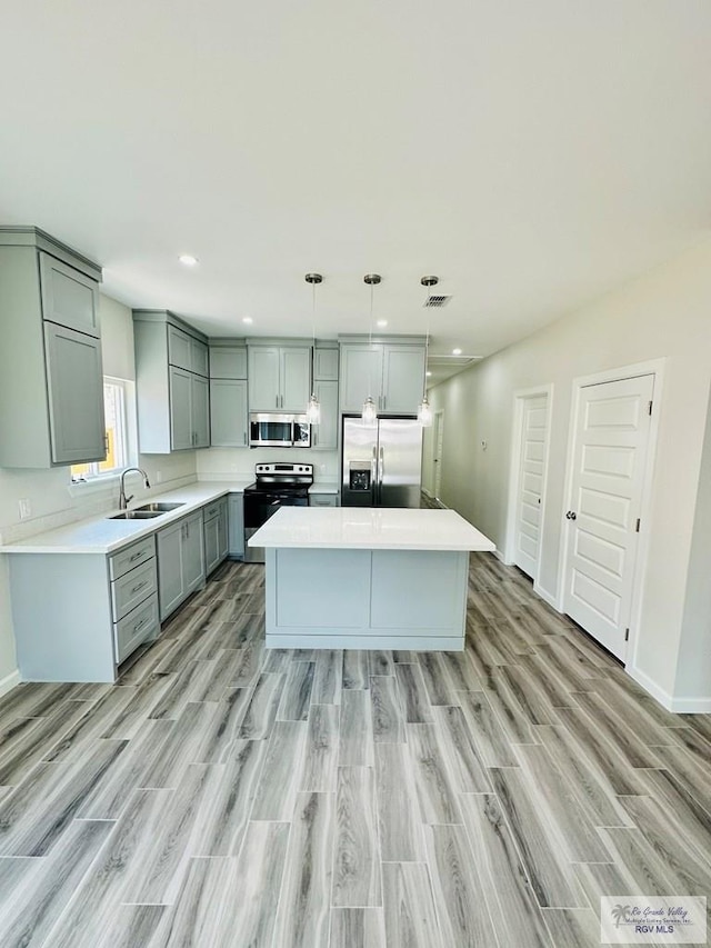 kitchen with appliances with stainless steel finishes, sink, decorative light fixtures, light hardwood / wood-style flooring, and a kitchen island