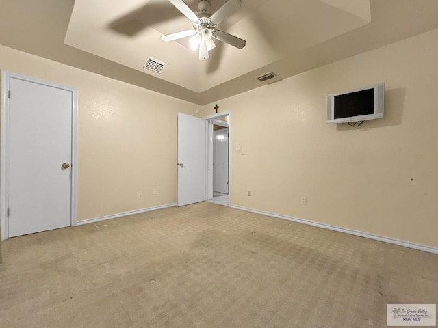 carpeted empty room with ceiling fan and a tray ceiling