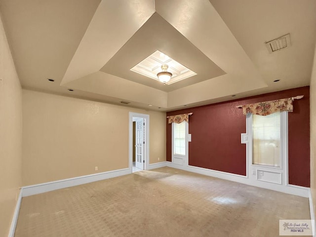 empty room with a tray ceiling, a skylight, and carpet