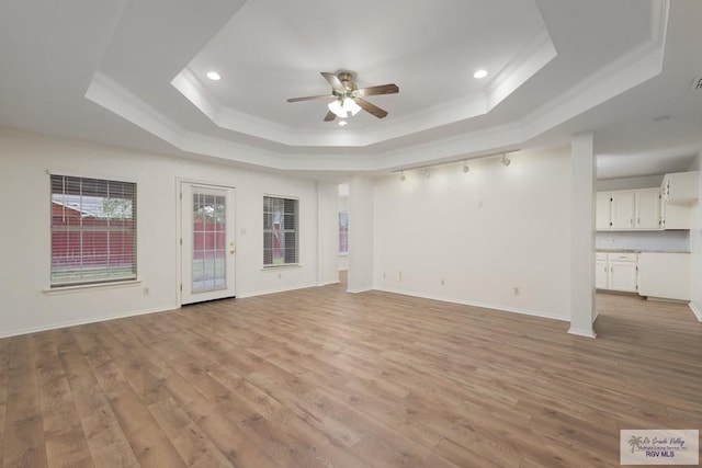 unfurnished living room featuring a tray ceiling, light wood finished floors, ornamental molding, a ceiling fan, and baseboards