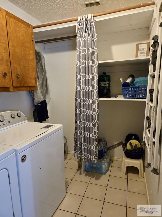 clothes washing area with cabinets, independent washer and dryer, a textured ceiling, and light tile patterned floors