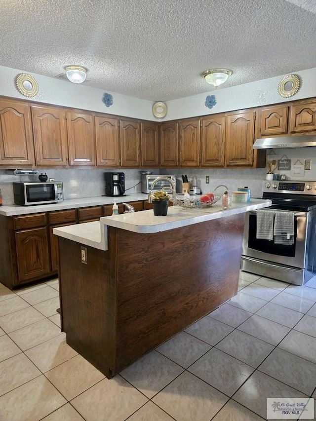 kitchen with a textured ceiling, a kitchen island, light tile patterned floors, and stainless steel range with electric cooktop