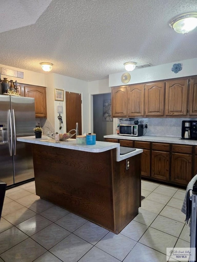 kitchen with stainless steel fridge with ice dispenser, light tile patterned floors, a textured ceiling, and a kitchen island