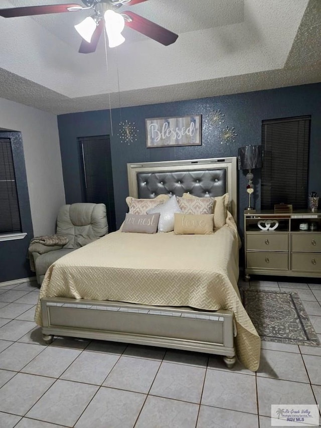 tiled bedroom featuring a textured ceiling, a tray ceiling, and ceiling fan