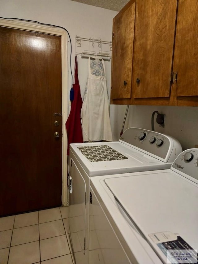 laundry area with cabinets, light tile patterned floors, a textured ceiling, and washing machine and clothes dryer