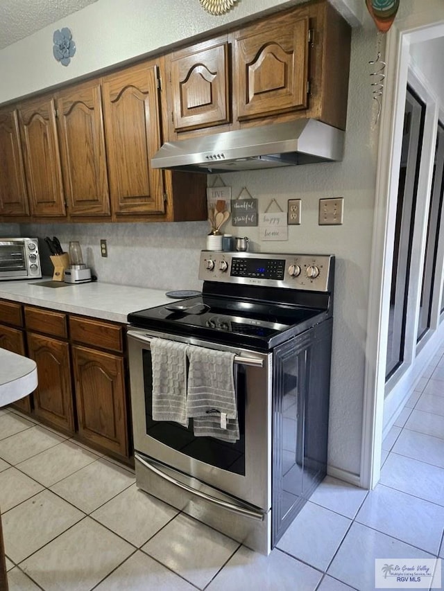 kitchen with light tile patterned floors, electric range, and a textured ceiling