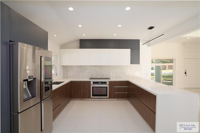 kitchen with pendant lighting, lofted ceiling, kitchen peninsula, white cabinetry, and stainless steel appliances