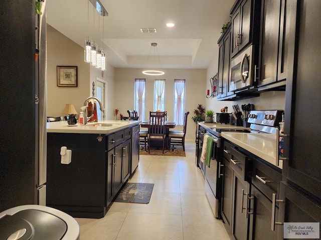 kitchen with stainless steel appliances, a tray ceiling, sink, pendant lighting, and an island with sink