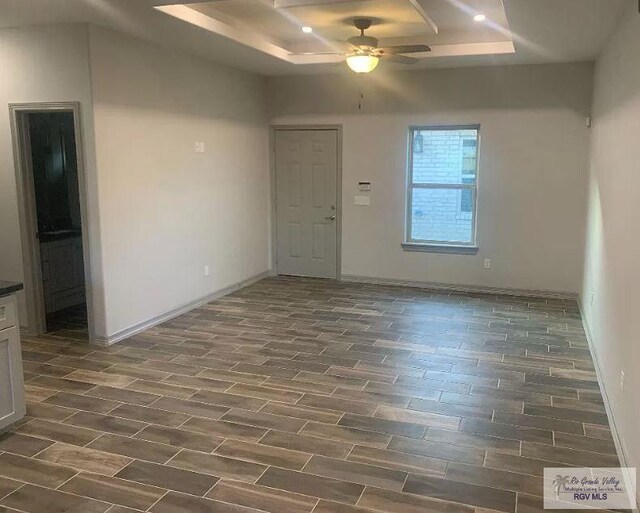 spare room with a tray ceiling, ceiling fan, and dark wood-type flooring