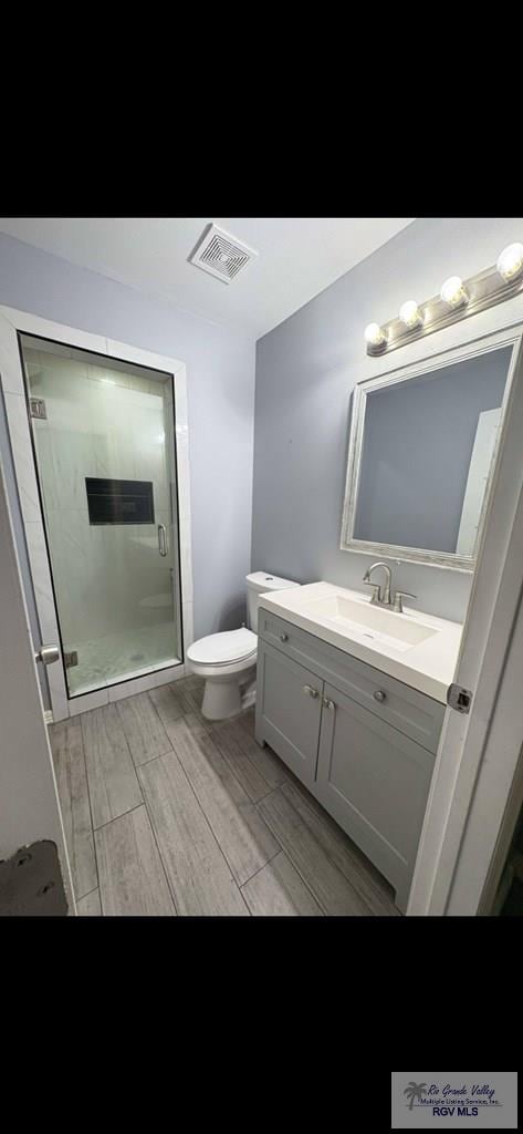 702 S California St, Harlingen, TX 78552 - full bathroom featuring vanity, toilet, wood finished floors, and a stall shower