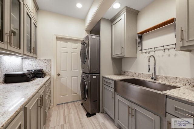 kitchen featuring gray cabinetry, backsplash, sink, light stone countertops, and stacked washer / drying machine