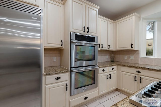 kitchen with light stone countertops, appliances with stainless steel finishes, tasteful backsplash, and light tile patterned flooring