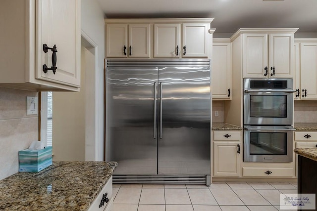 kitchen featuring light tile patterned floors, cream cabinetry, stone countertops, and appliances with stainless steel finishes