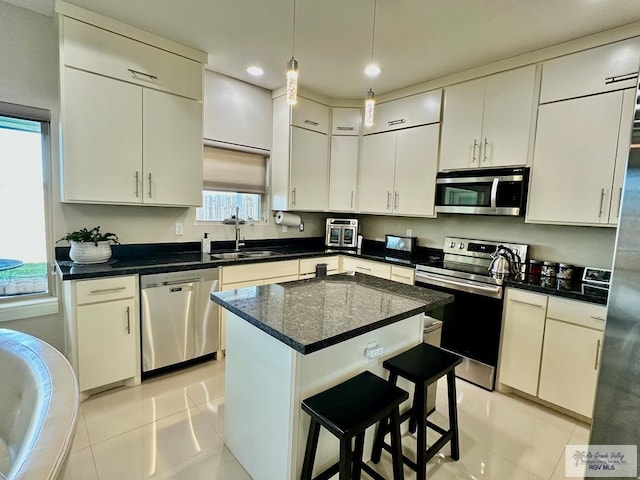 kitchen featuring a breakfast bar area, light tile patterned flooring, a sink, appliances with stainless steel finishes, and decorative light fixtures