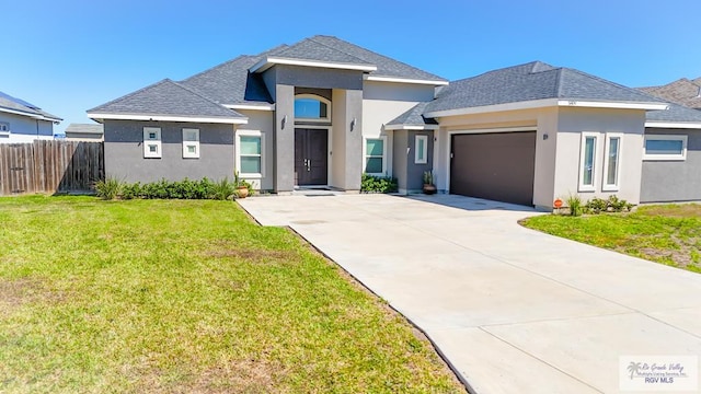 view of front of property featuring an attached garage, fence, a front lawn, and stucco siding