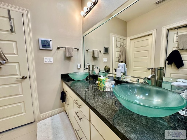 full bath featuring baseboards, double vanity, a sink, and tile patterned floors