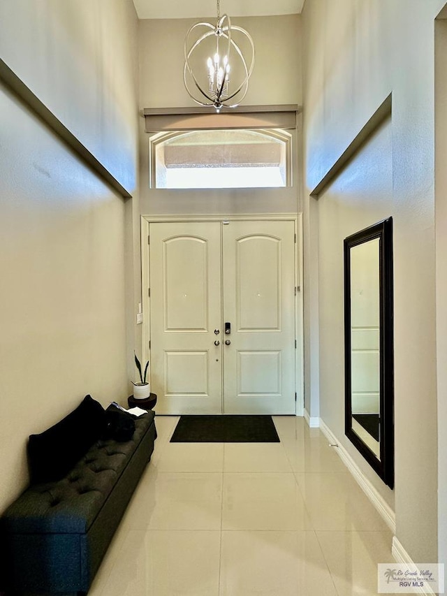 tiled entrance foyer featuring a chandelier, a towering ceiling, and baseboards