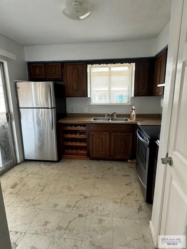 kitchen with a textured ceiling, dark brown cabinetry, sink, and appliances with stainless steel finishes