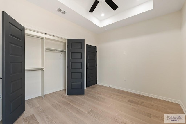 unfurnished bedroom with ceiling fan, light hardwood / wood-style floors, a tray ceiling, and a closet