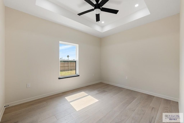 spare room with light hardwood / wood-style floors, a raised ceiling, and ceiling fan