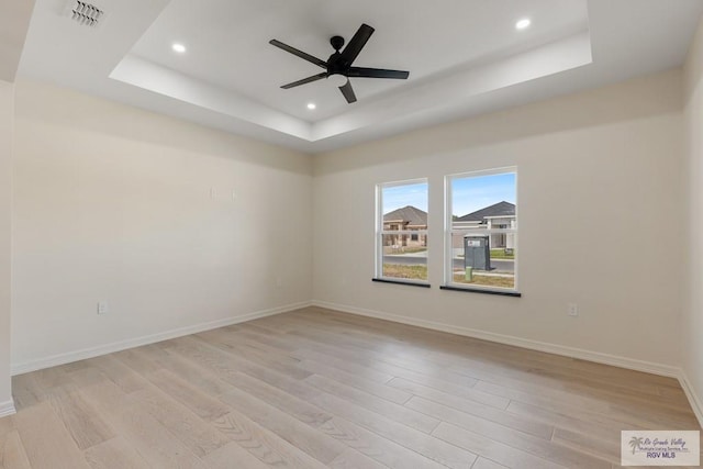 unfurnished room with ceiling fan, a raised ceiling, and light wood-type flooring