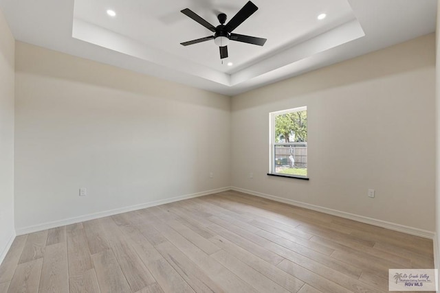 empty room with ceiling fan, light hardwood / wood-style flooring, and a tray ceiling