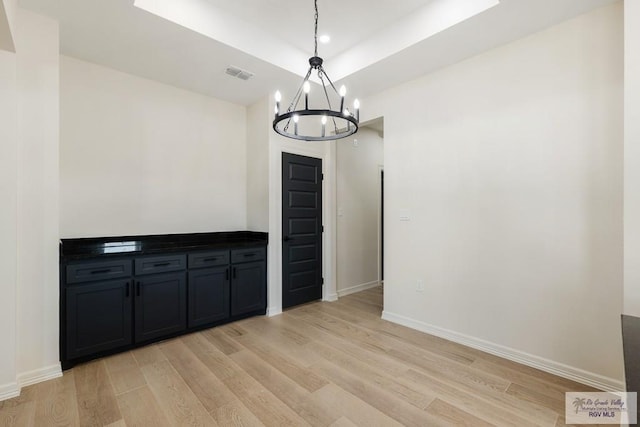 unfurnished dining area with a tray ceiling, light hardwood / wood-style floors, and a notable chandelier